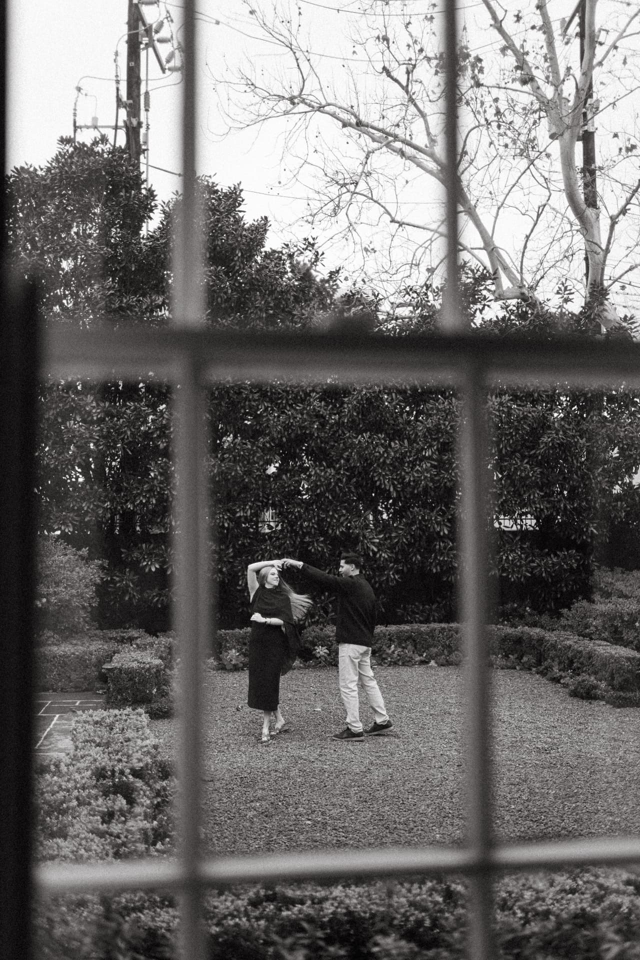 Wasi and Hope dancing in the garden, seen through an architectural window in black and white