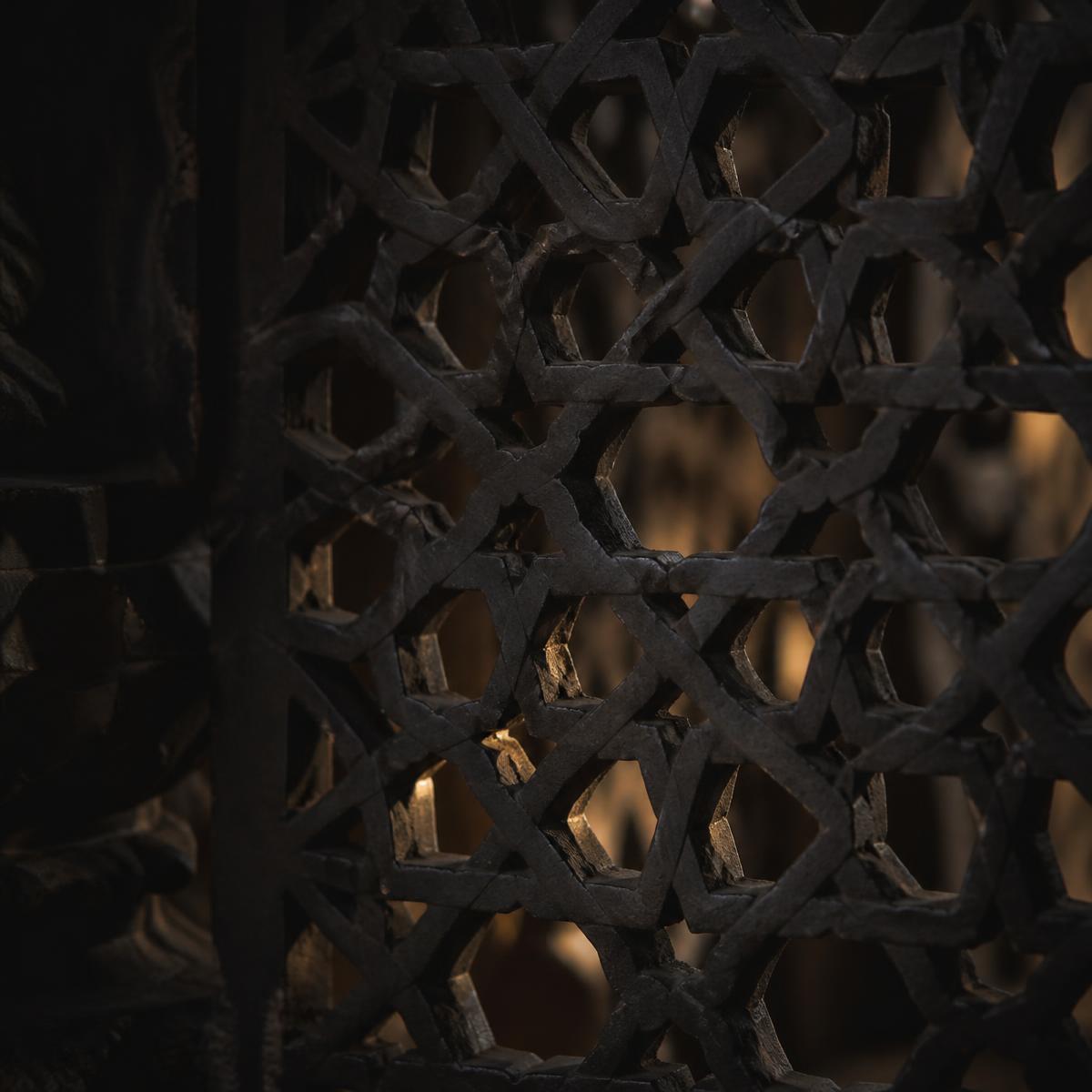 A carved jaali screen in near-darkness with candlelight passing through the lattice