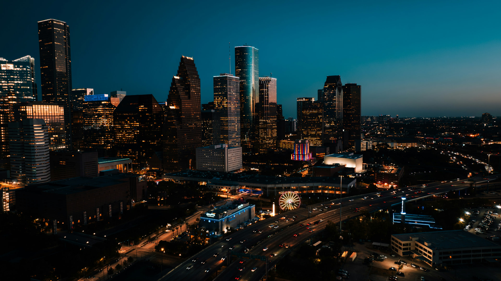 The downtown Houston skyline at dusk, with a warm horizon and freeway light trails