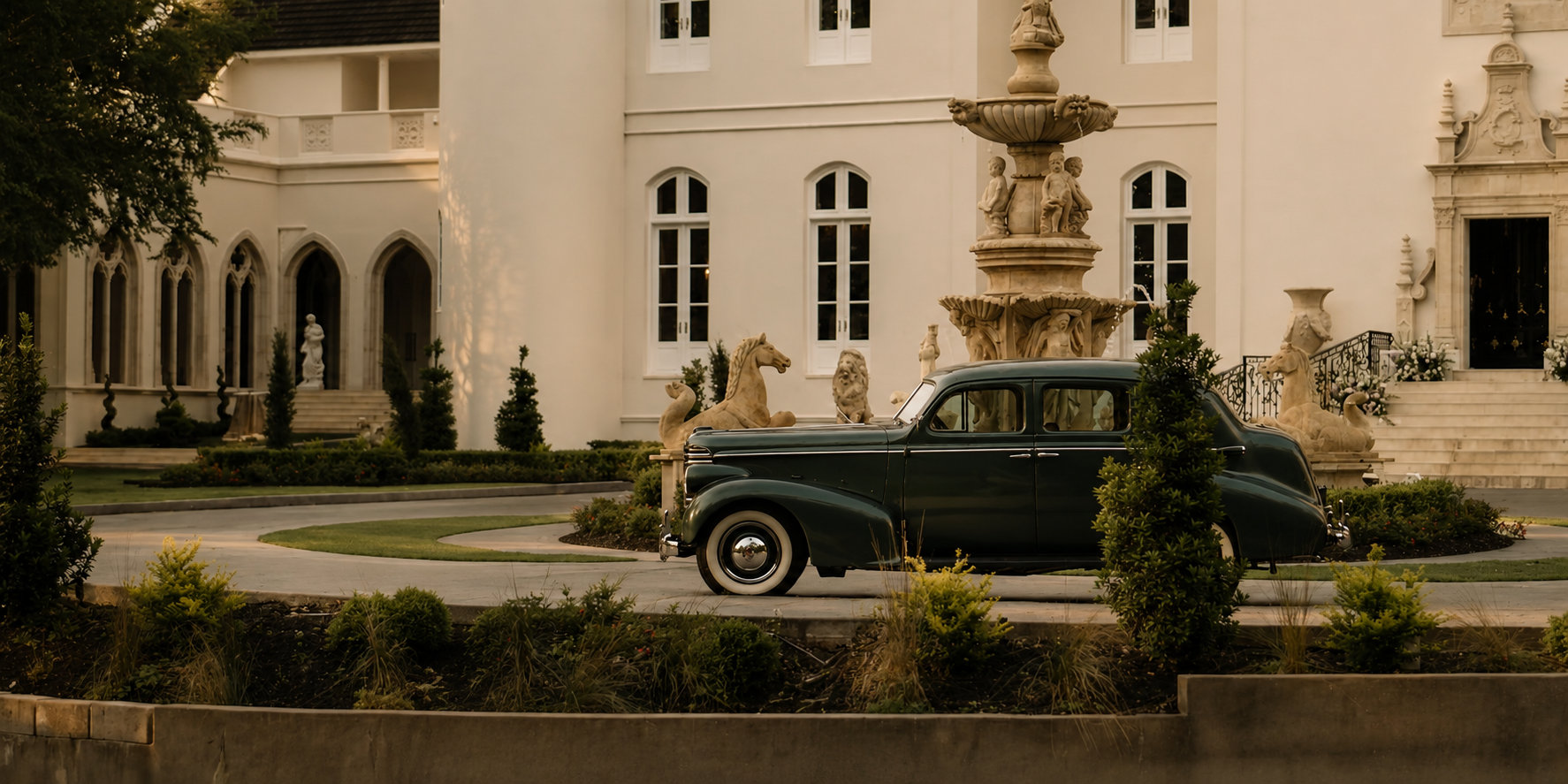 A deep green vintage car parked at the Chateau Nouvelle fountain court
